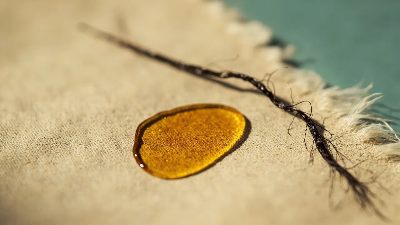 Mechón de cabello sobre superficie neutra con una gota dorada que representa hierro almacenado.