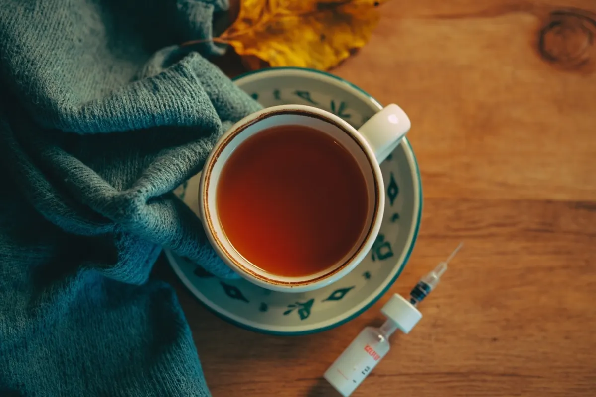 Bufanda turquesa doblada, taza de té caliente y hojas de otoño sobre una mesa de madera, simbolizando la protección frente a la gripe.